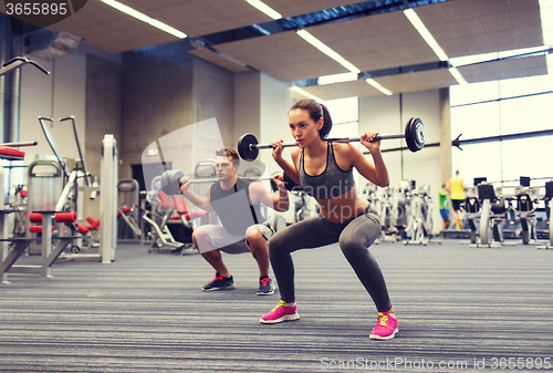 Image of young man and woman training with barbell in gym