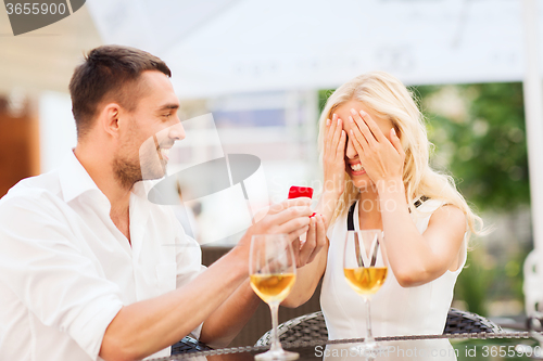 Image of happy couple with engagement ring and wine at cafe