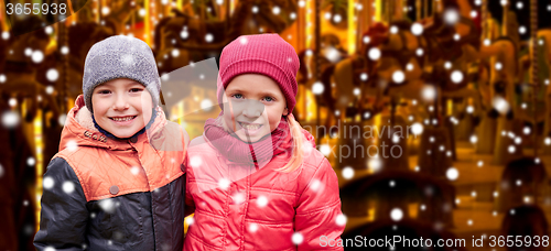 Image of little girl hugging boy over snow and carousel