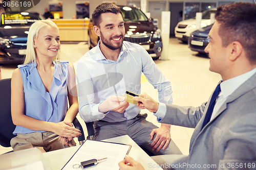 Image of happy couple with car dealer in auto show or salon