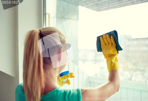 Image of happy woman in gloves cleaning window with rag