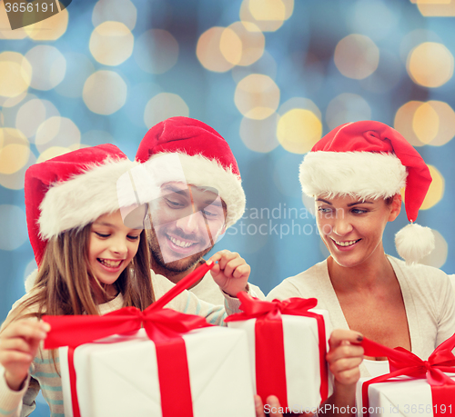 Image of happy family in santa hats sitting with gift boxes