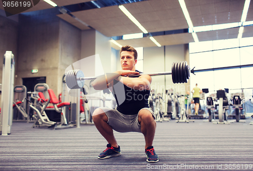 Image of young man flexing muscles with barbell in gym