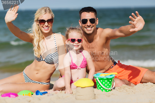 Image of happy family with sand toys waving hands on beach