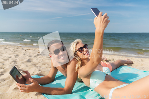 Image of happy couple with modern gadgets lying on beach