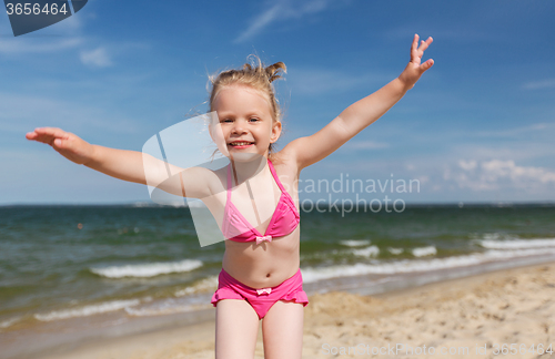 Image of happy little girl in swimwear having fun on beach