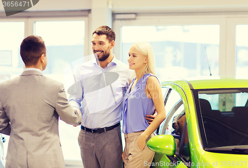 Image of happy couple with car dealer in auto show or salon