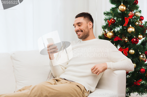 Image of smiling man with smartphone at home for christmas