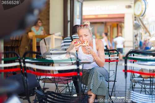 Image of Woman eating pizza outdoor in cafeteria.