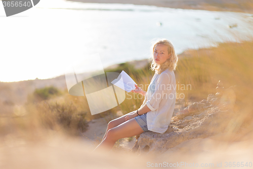 Image of Woman enjoys reading on beautiful sandy beach.