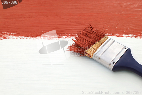 Image of Paintbrush with red paint, painting over white board
