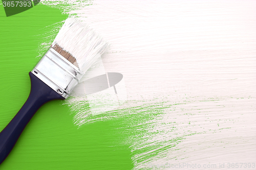 Image of Paintbrush with white paint painting over green