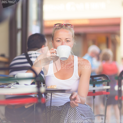 Image of Woman drinking coffee outdoor on street.
