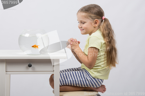 Image of Four-year girl makes a wish sitting in front of a goldfish