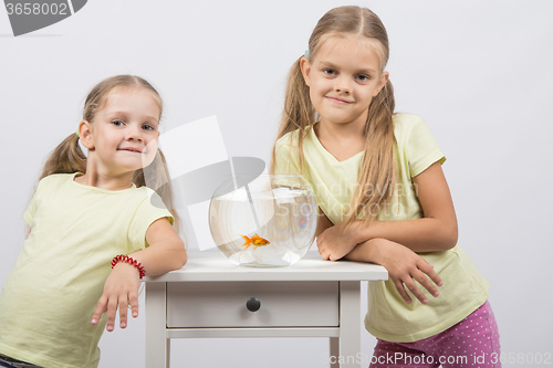 Image of Two sisters stand at the small fishbowl with goldfish