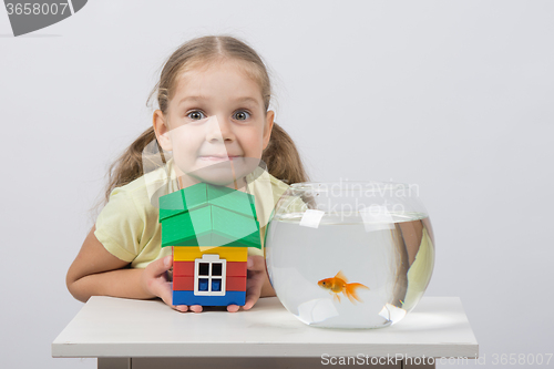 Image of Four-year girl holding a toy house and sits in front of a goldfish