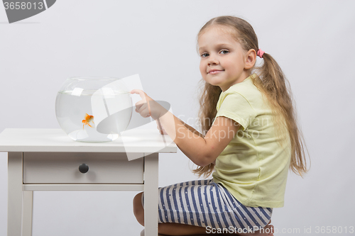 Image of Four-year girl sitting in front of an aquarium with goldfish and knocks his finger on it