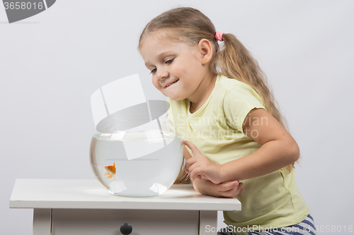 Image of Four-year girl smiling looking at a goldfish in an aquarium