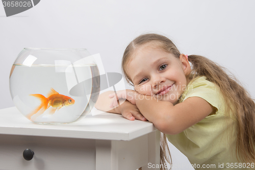 Image of Happy four-year girl put her head in his hands sitting in front of a goldfish