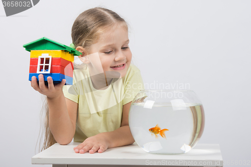 Image of The four-year girl sits with a toy house in front of a goldfish