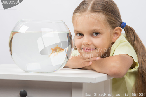 Image of Six year old girl put her head on the handle sitting at the table with an aquarium with goldfish