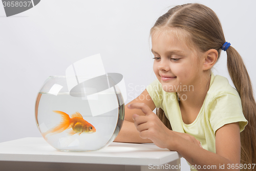 Image of Happy little girl knocking his finger on the aquarium with goldfish