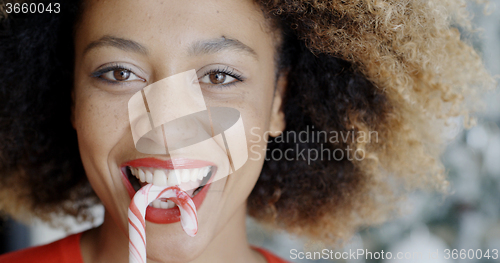 Image of Fun young woman biting Christmas candy cane