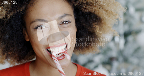 Image of Fun young woman biting Christmas candy cane
