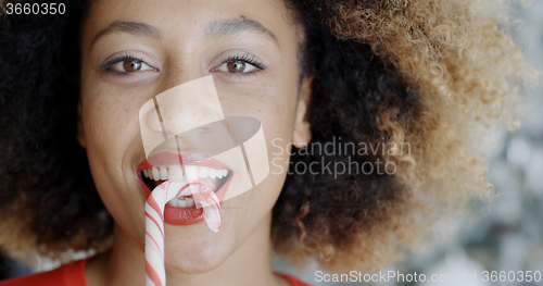 Image of Fun young woman biting Christmas candy cane