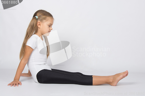 Image of Girl gymnast sitting on the floor and looks at her outstretched legs
