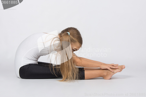 Image of Girl gymnast performs a tuck sitting on the floor pulls hands to toes