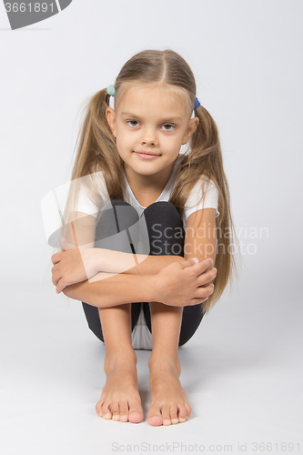 Image of Girl gymnast sitting on the floor hugging his legs