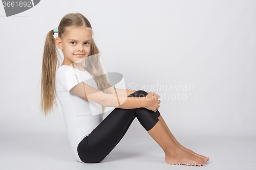 Image of Gymnast six years sitting hugging her knees legs