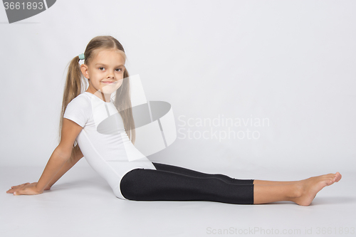 Image of Girl gymnast sitting on the floor with legs stretched and leaned back on his hands