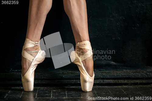 Image of Close-up ballerina\'s legs in pointes on the black wooden floor 