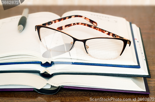 Image of Glasses, books and notebook on the table surface.