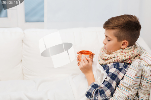 Image of ill boy with flu in scarf drinking tea at home