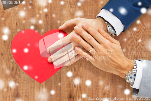 Image of close up of male gay couple hands with red heart