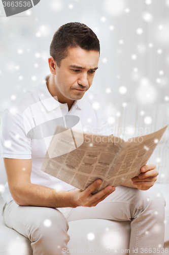 Image of sad man reading newspaper at home