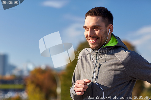 Image of happy man with earphones running in city