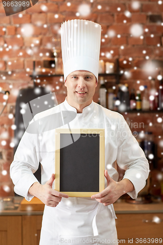 Image of happy male chef with blank menu board in kitchen