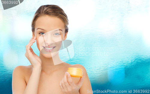 Image of happy young woman applying cream to her face