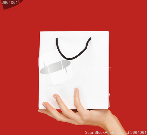 Image of close up of hand holding white bag over red