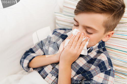 Image of ill boy lying in bed and blowing his nose at home