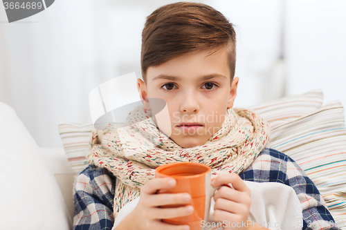 Image of ill boy with flu in scarf drinking tea at home