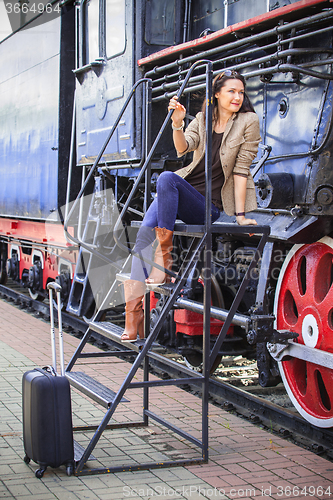 Image of pretty middle-aged woman with luggage near the old steam locomot