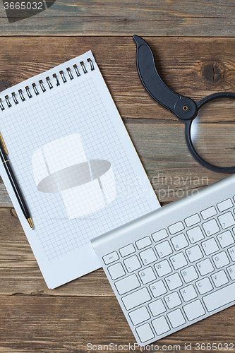 Image of Computer keyboard, notebook, pen and magnifying glass