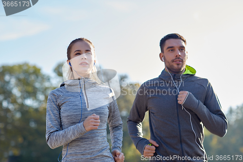 Image of happy couple with earphones running outdoors