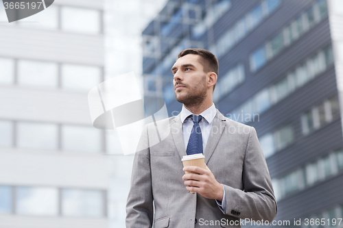 Image of young serious businessman with paper cup outdoors