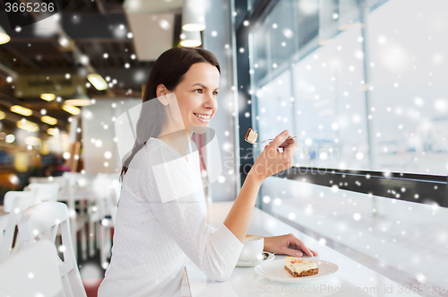 Image of smiling young woman with cake and coffee at cafe